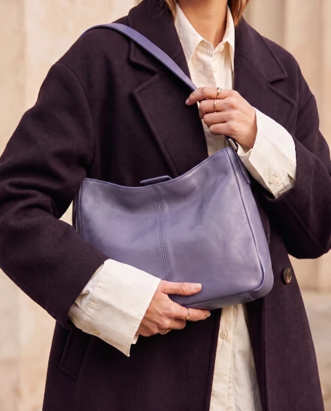 Close-up of a lavender shoulder bag with a dark plum coat, ivory shirt cuffs and gold rings.
